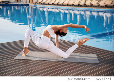 Busy by doing yoga exercise. Fitness woman is near the pool 132261661