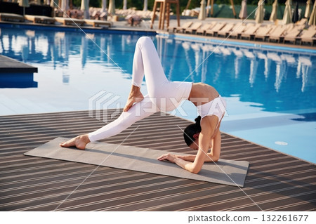 Busy by doing yoga exercise. Fitness woman is near the pool Busy by doing yoga exercise. Fitness woman is near the pool 132261677