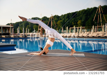 White clothes, side view, doing yoga. Fitness woman is near the pool White clothes, side view, doing yoga. Fitness woman is near the pool 132261703