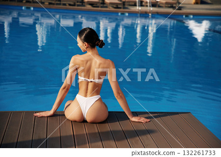 Back view, sitting. Beautiful woman in bikini is resting by the pool Back view, sitting. Beautiful woman in bikini is resting by the pool 132261733