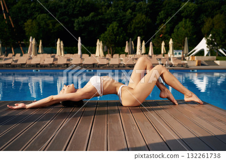 Side view, lying down. Beautiful woman in bikini is resting by the pool Side view, lying down. Beautiful woman in bikini is resting by the pool 132261738
