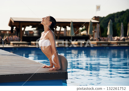 Positive vibes. Beautiful woman in bikini is resting by the pool 132261752
