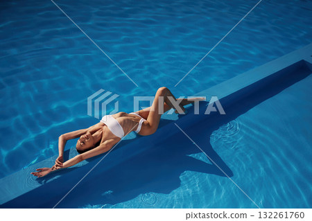 View from the top, lying down. Beautiful woman in bikini is resting by the pool View from the top, lying down. Beautiful woman in bikini is resting by the pool 132261760