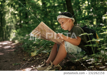 Little kid tourist is sitting and reading the map in the forest 132262158