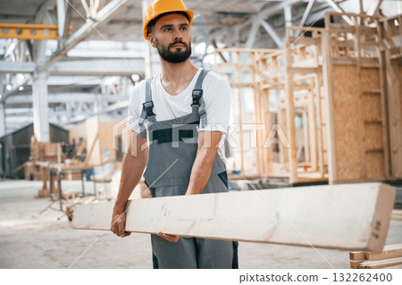 Front view, holding plank. Industrial worker in wooden warehouse 132262400