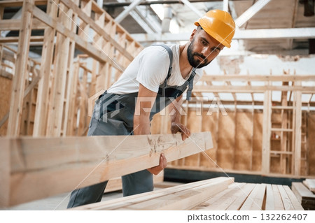 Front view, holding plank. Industrial worker in wooden warehouse Front view, holding plank. Industrial worker in wooden warehouse 132262407