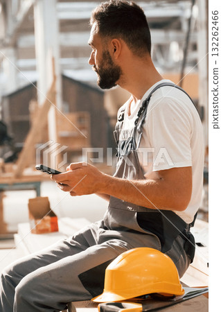 Taking a rest, sitting with smartphone. Industrial worker in wooden warehouse 132262466