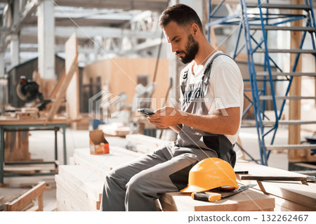 Taking a rest, sitting with smartphone. Industrial worker in wooden warehouse 132262467