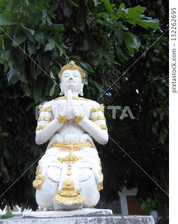 White Statue with Golden Ornaments Kneeling in Prayer Under a Lush Tree White Statue with Golden Ornaments Kneeling in Prayer Under a Lush Tree 132262695