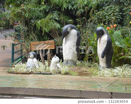 Penguin Statues with a Signboard at the Lush Zoo Entrance Surrounded by Plants 132263054
