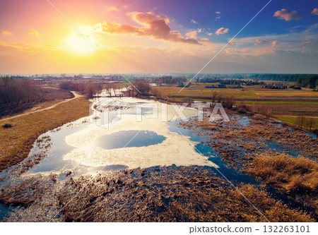 Aerial view of the countryside and frozen winding brook in the evening at sunset light. Beautiful natural landscape with cloudy sky 132263101