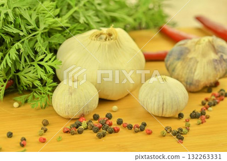 A bulb of garlic, red chili peppers, four-color pepper, and carrot tops on a wooden cutting board. The concept of culinary arts and vegetables in the home. Macro image, close-up. Garlic - species 132263331