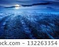 landscape with dirt road through field in fog in summer at night. yellow grass on the hills under dark sky in full moon light. mystery atmosphere countryside composite photo 132263354