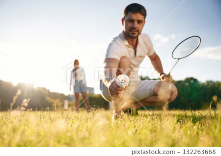 Fallen shuttlecock, guy is taking it. Man with woman are playing badminton on the field Fallen shuttlecock, guy is taking it. Man with woman are playing badminton on the field 132263668