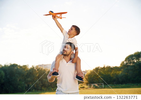 Sitting on man's shoulders, with toy plane. Father and little son are together on the summer field Sitting on man's shoulders, with toy plane. Father and little son are together on the summer field 132263771