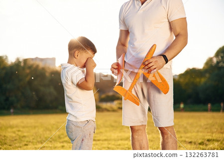 Broken toy plane, boy is crying. Father and little son are together on the summer field Broken toy plane, boy is crying. Father and little son are together on the summer field 132263781