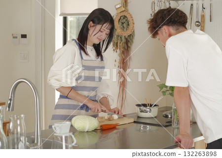一名男子正與一名繫著圍裙做飯的女子愉快地交談 一名男子正與一名繫著圍裙做飯的女子愉快地交談 132263898