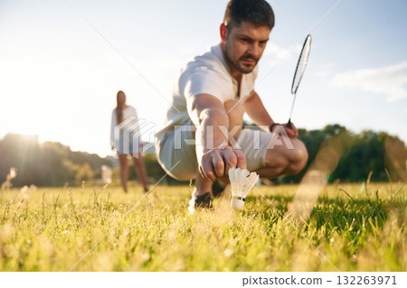 Fallen shuttlecock, guy is taking it. Man with woman are playing badminton on the field Fallen shuttlecock, guy is taking it. Man with woman are playing badminton on the field 132263971