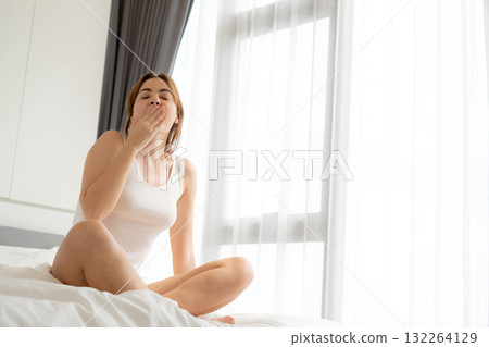 Young caucasian woman sleepy yawning in bed after wake up in morning in bedroom at home. 132264129
