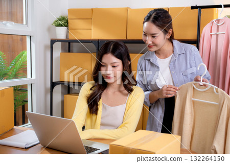 Two young asian businesswoman checking order clothes of customer for laptop. Two young asian businesswoman checking order clothes of customer for laptop. 132264150