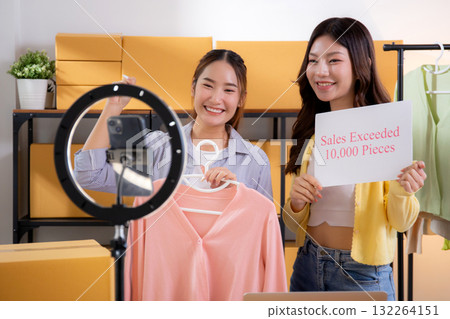 Two asian woman live streaming online clothing store while showing clothing with smartphone. Two asian woman live streaming online clothing store while showing clothing with smartphone. 132264151