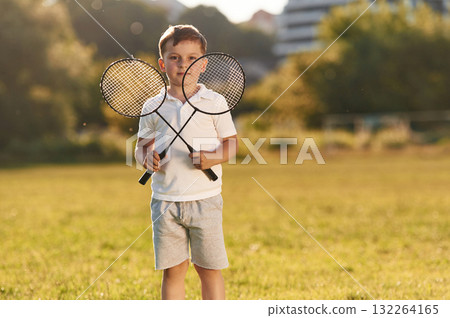 Happy little boy is with two tennis or badminton rackets on the summer field 132264165