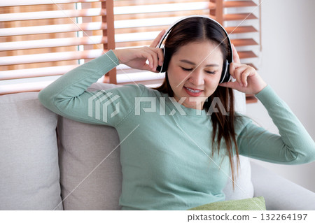Happy young asian woman wearing headphones listening music while sitting on sofa with fun. Happy young asian woman wearing headphones listening music while sitting on sofa with fun. 132264197