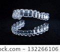 Close-up shot of transparent dental aligners, used for teeth alignment, against a stark black backdrop. The clear retainers are designed to gradually shift teeth. 132266106