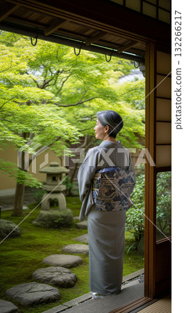 A Japanese woman in a kimono looks out at the garden from the veranda, green maple leaves 132266217