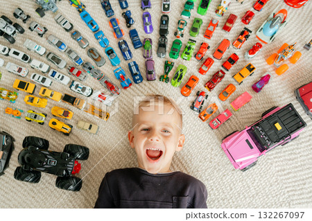 Energetic child smiles widely while surrounded by dozens of miniature vehicles on carpet, vibrant toys and fun mood Energetic child smiles widely while surrounded by dozens of miniature vehicles on carpet, vibrant toys and fun mood 132267097