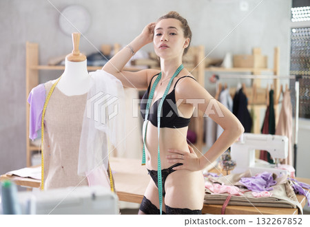 Sexy seamstress girl in black stockings and bra tries on dress on mannequin 132267852