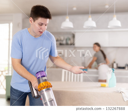 Guy collects dust with vacuum cleaner during group cleaning in kitchen Guy collects dust with vacuum cleaner during group cleaning in kitchen 132267888