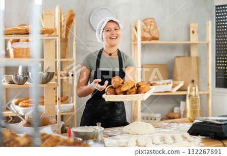 Positive female baker in uniform holding basket with croissants Positive female baker in uniform holding basket with croissants 132267891