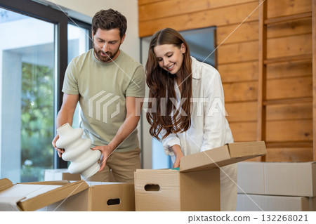 Excited couple unpacking boxes in their new home and feeling joyful Excited couple unpacking boxes in their new home and feeling joyful 132268021