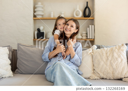 Daughter hugging her smiling mother while sitting together in warm family space on sofa Daughter hugging her smiling mother while sitting together in warm family space on sofa 132268169