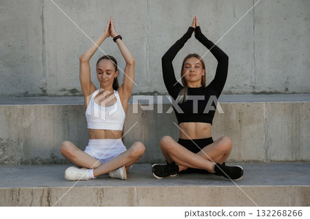 In lotus pose, yoga. Two sportive women are outdoors together In lotus pose, yoga. Two sportive women are outdoors together 132268266