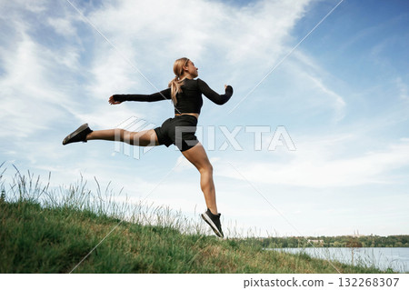 Jumping against the sky. Beautiful fitness woman in sport clothes is outdoors Jumping against the sky. Beautiful fitness woman in sport clothes is outdoors 132268307