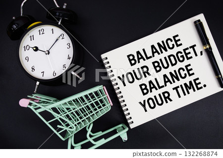 Balance Your Budget, Balance Your Time text written on notepad with alarm clock and trolley shopping cart on black background 132268874