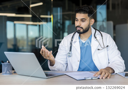 Male doctor wearing a white coat and stethoscope providing medical advice during an online consultation on a laptop, using digital healthcare technology in a modern office setting Male doctor wearing a white coat and stethoscope providing medical advice during an online consultation on a laptop, using digital healthcare technology in a modern office setting 132269024