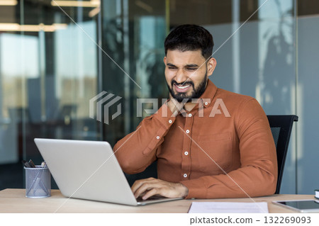 Young businessman experiencing severe neck pain and discomfort while working long hours on his laptop in a modern office, highlighting work-related stress and poor ergonomics Young businessman experiencing severe neck pain and discomfort while working long hours on his laptop in a modern office, highlighting work-related stress and poor ergonomics 132269093