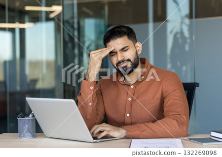 Young businessman experiencing a painful headache and severe eyestrain while working long hours on a laptop in a modern office, symbolizing stress, overwork, and burnout in professional life Young businessman experiencing a painful headache and severe eyestrain while working long hours on a laptop in a modern office, symbolizing stress, overwork, and burnout in professional life 132269098