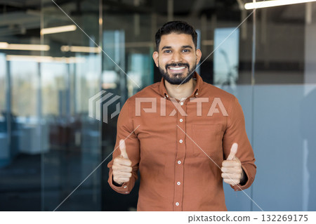 Young indian businessman showing a positive gesture and smiling at the camera, conveying success, approval, and confidence in a modern office environment 132269175