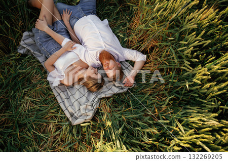 On the blanket, lying down, top view. Lovely couple are on the green agricultural field together On the blanket, lying down, top view. Lovely couple are on the green agricultural field together 132269205