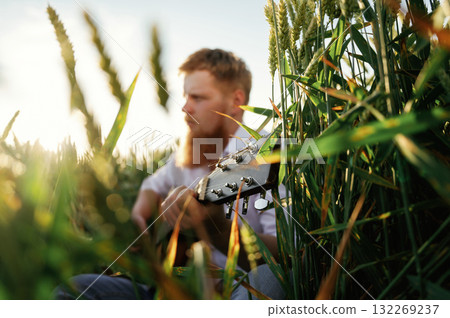Country musician is with guitar on the ground. Man in white shirt is on the agricultural field Country musician is with guitar on the ground. Man in white shirt is on the agricultural field 132269237