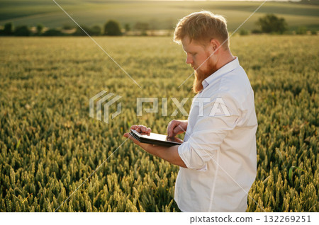 Black digital tablet. Man in white shirt is on the agricultural field 132269251