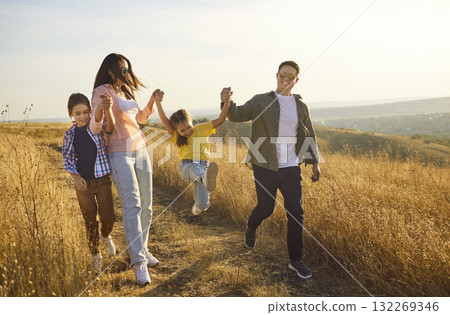 Happy family walking along path through meadow, enjoying nature at sunset Happy family walking along path through meadow, enjoying nature at sunset 132269346
