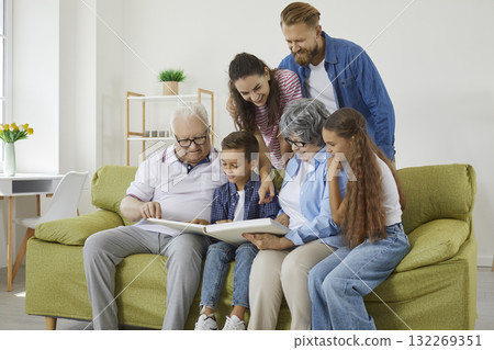 Family looks at photo album together and remembers stories from past during reunion of relatives. 132269351