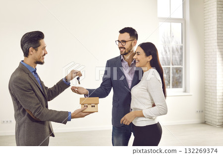 Real estate agent giving house key to a young happy smiling couple customers. Real estate agent giving house key to a young happy smiling couple customers. 132269374