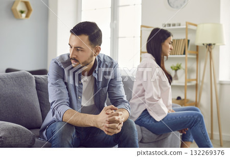Sad young attractive family together at home in cozy living room, sitting on different sides of the sofa with their backs to each other. Quarrel, resentment, anger, insult, bitterness, discontent. Sad young attractive family together at home in cozy living room, sitting on different sides of the sofa with their backs to each other. Quarrel, resentment, anger, insult, bitterness, discontent. 132269376