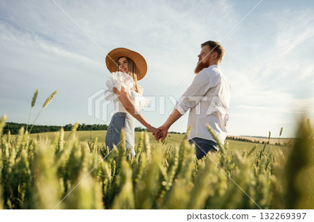 Holding each other's hands. Lovely couple are on the green agricultural field together 132269397